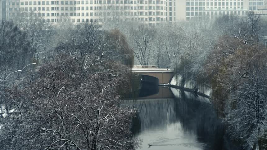 Cars and people traveling over a river bridge in a city during a snow storm