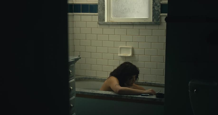 A woman is sitting motionless in a bathtub while holding a cigarette