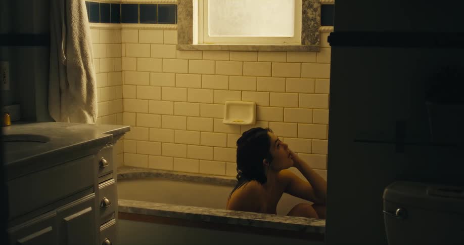 A woman jolts up from lying in a bathtub