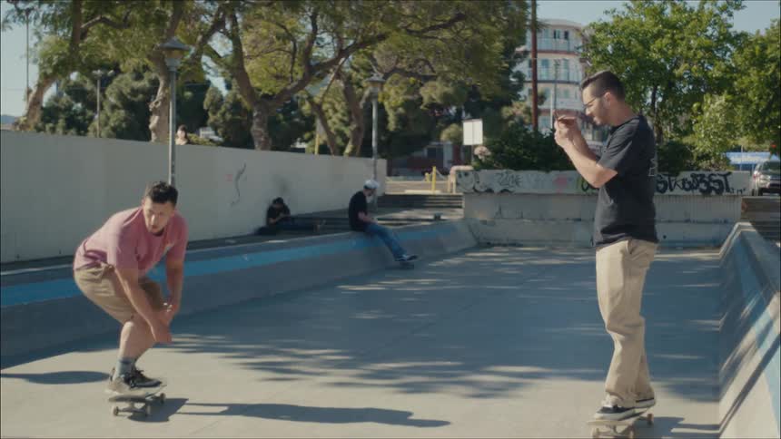 A man films someone with his cell phone doing a skate trick