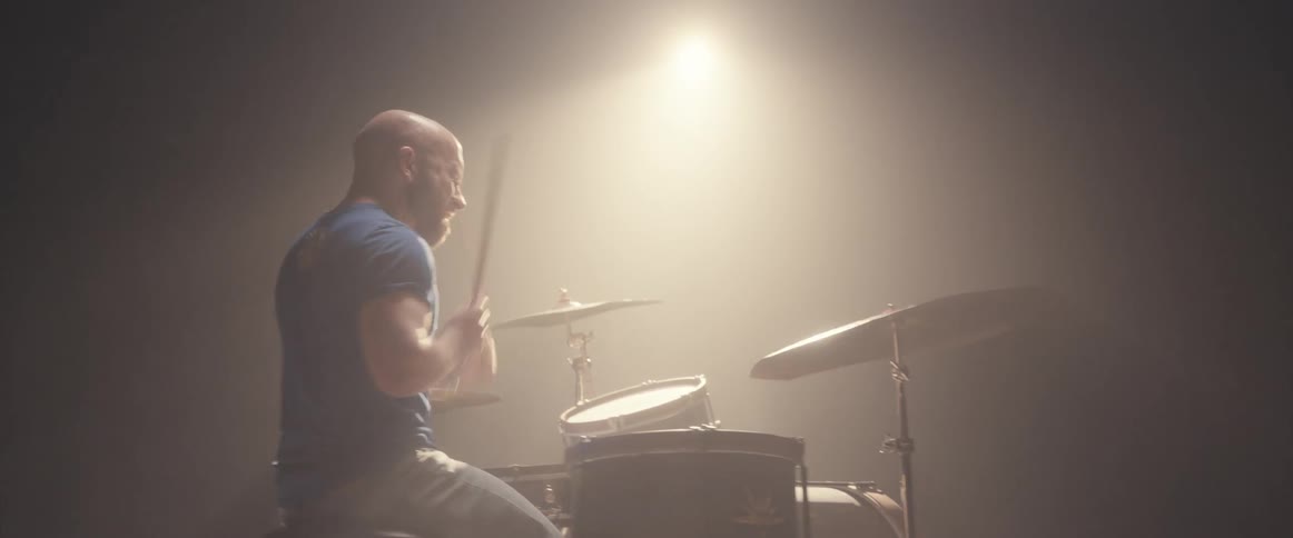 A man plays the drums under a bright spotlight