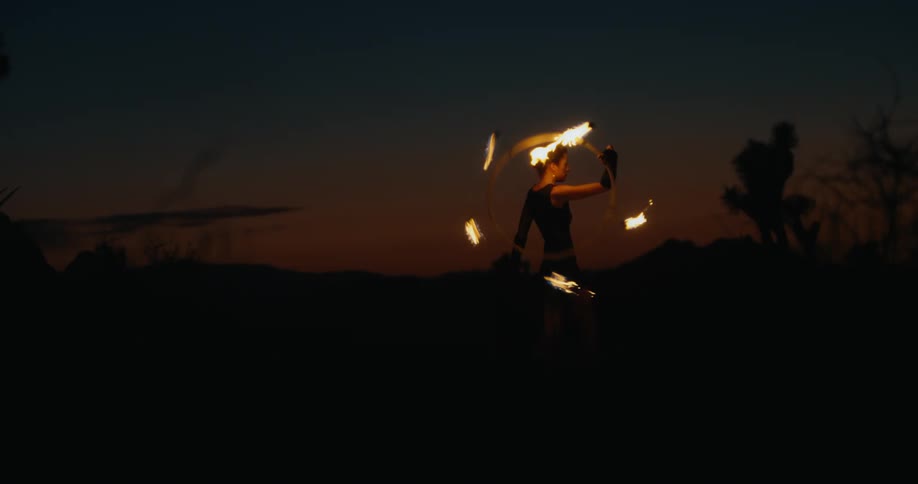 A woman stands in a field spinning a burning circle