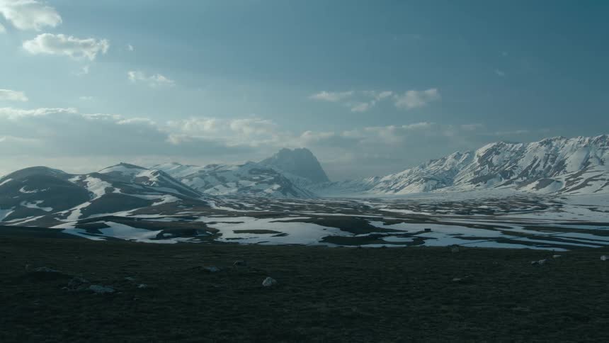 Timelapse of clouds rolling over the top of a mountain range covered in snow