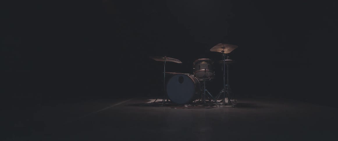 A spotlight shines on a drum kit on a stage and the light goes off
