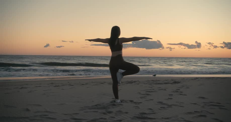 A woman is doing yoga on the beach at sunset