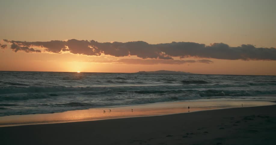 Ocean waves break against the shore at sunset