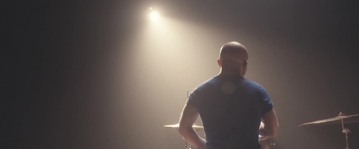 A man plays the drums with a spotlight shining on him