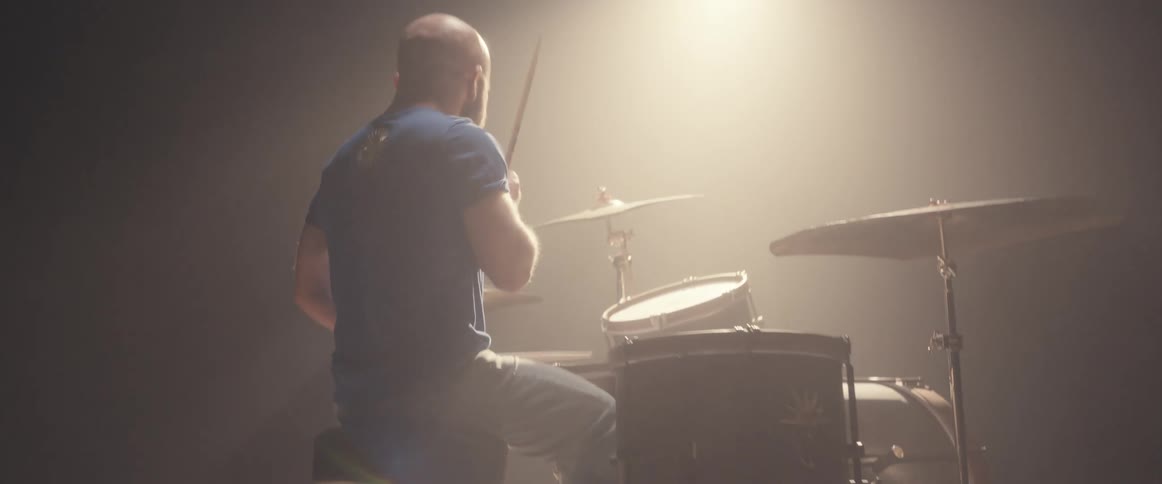 A man plays the drums under the spotlight