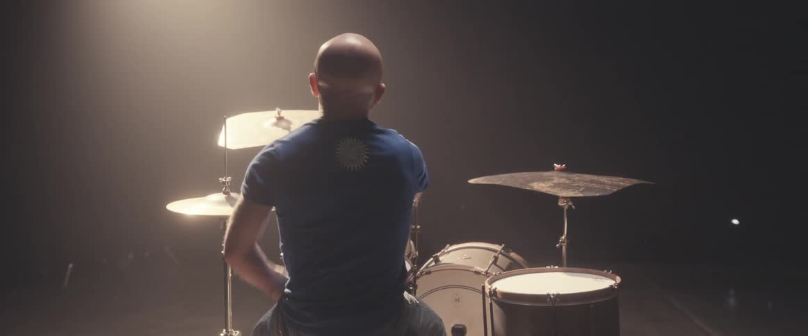 Bald male drummer with blue shirtjeans and beard plays drums in spotlight