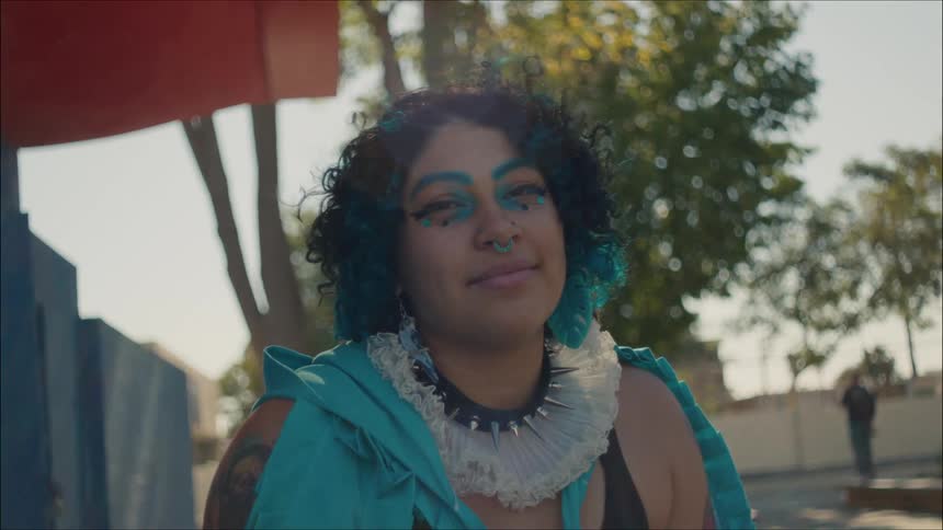 Young person wearing colorful makeup and nose ring sitting on a park