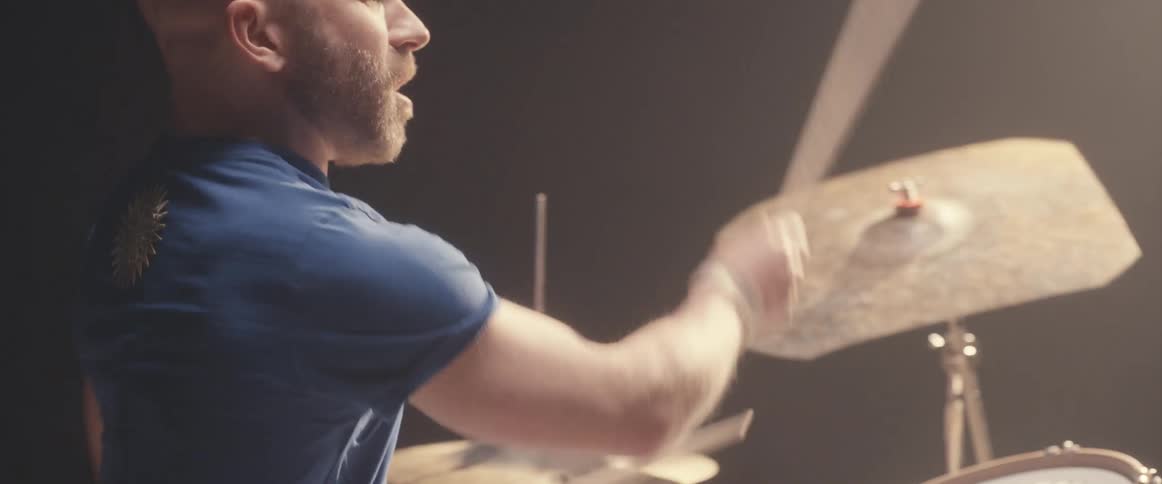 A man is holding drumsticks and playing the drums as a light shines above him