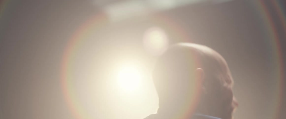 A man is holding drumsticks and playing the drums as a light shines above him