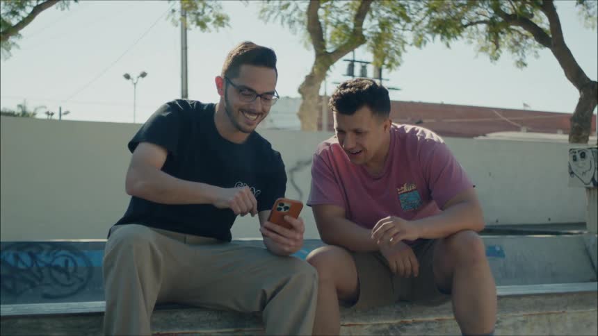 Two men are sitting on a park bench looking at something on a phone