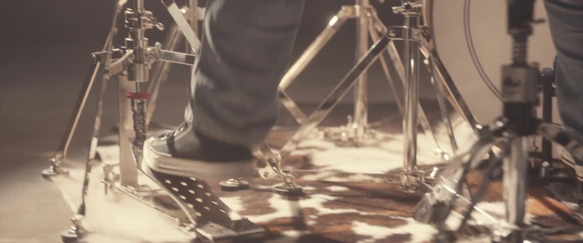A drummer is sitting on a stool and his feet are moving on the pedals as he plays the drums