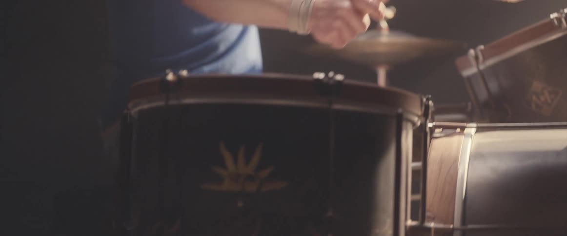 Bald male drummer with blue shirt and beard plays drums in spotlight