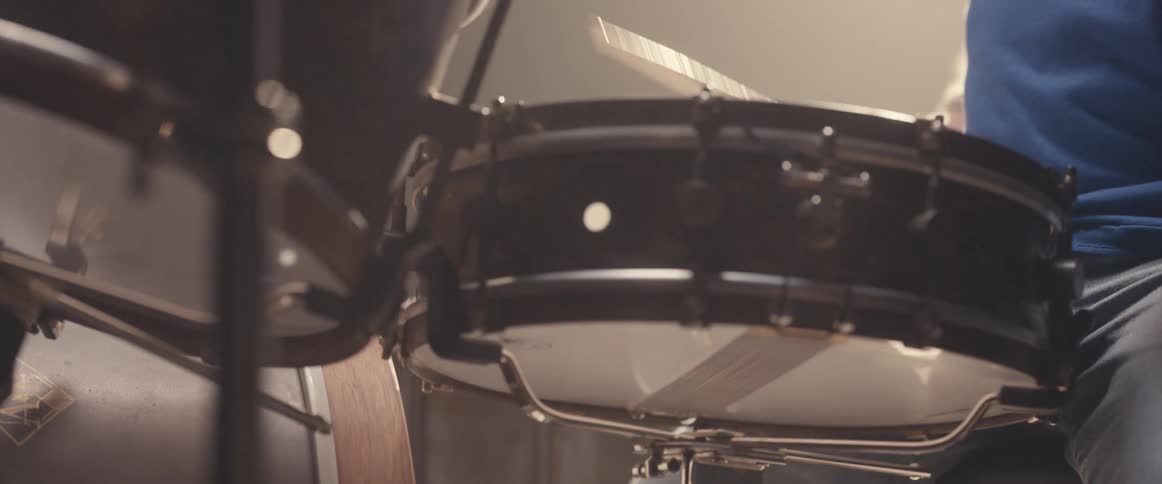 A man plays the drums under a spotlight in a dark place