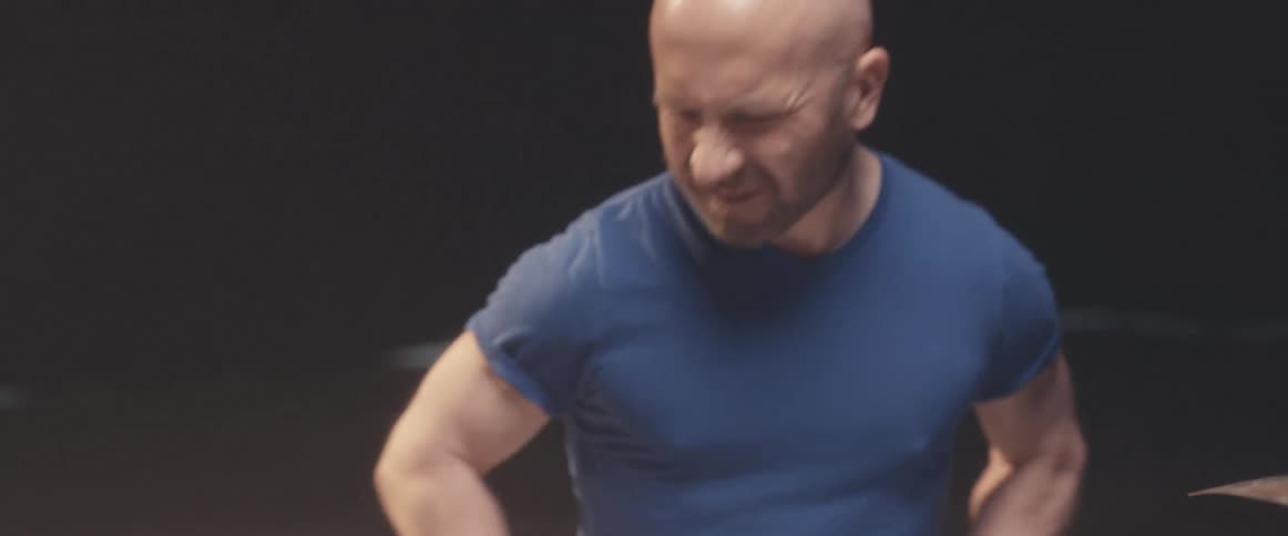 Bald muscular man playing drums on a stage under a spotlight