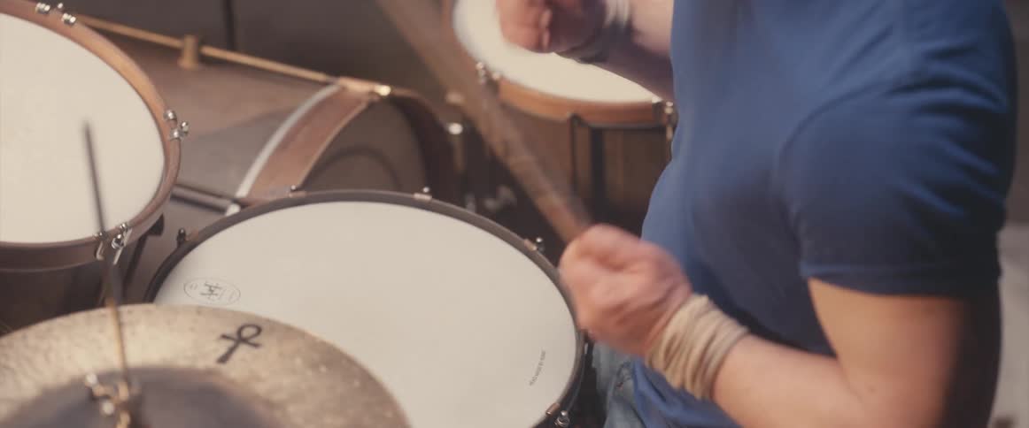 Man is playing a set of drums indoors