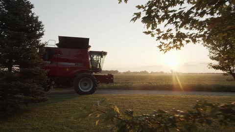 Farming machinery sits parked on driveway with crop fields stretching to the horizon