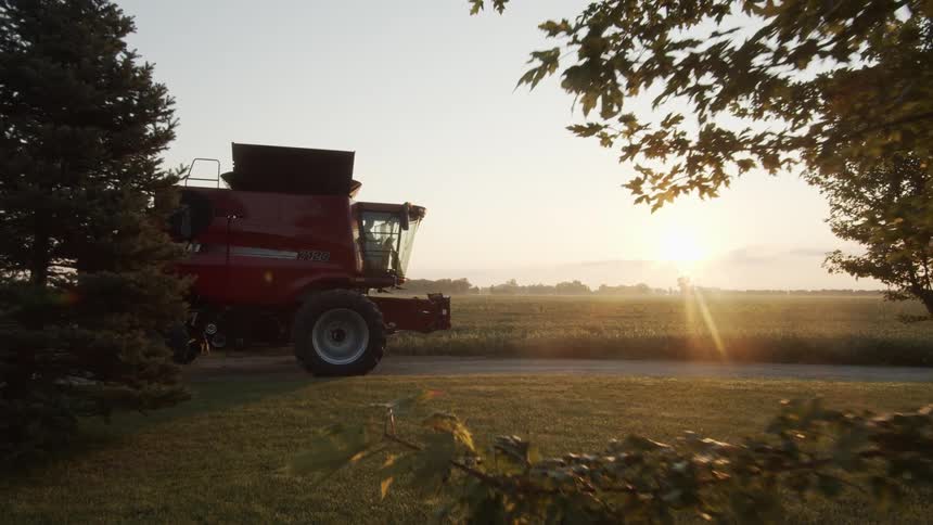 Farming machinery sits parked on driveway with crop fields stretching to the horizon