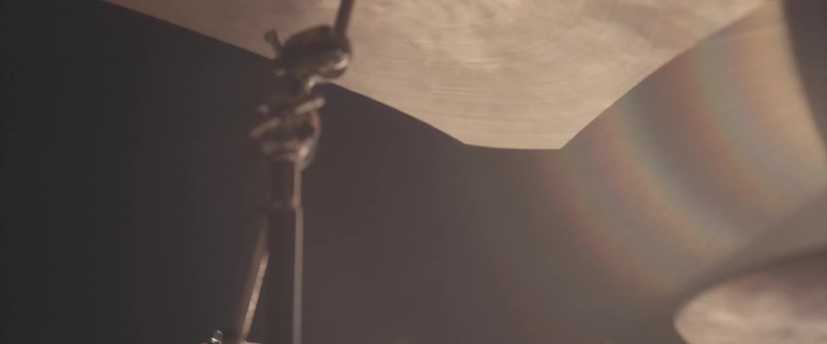 A man is holding drumsticks and playing the drums as a stage light shines on him