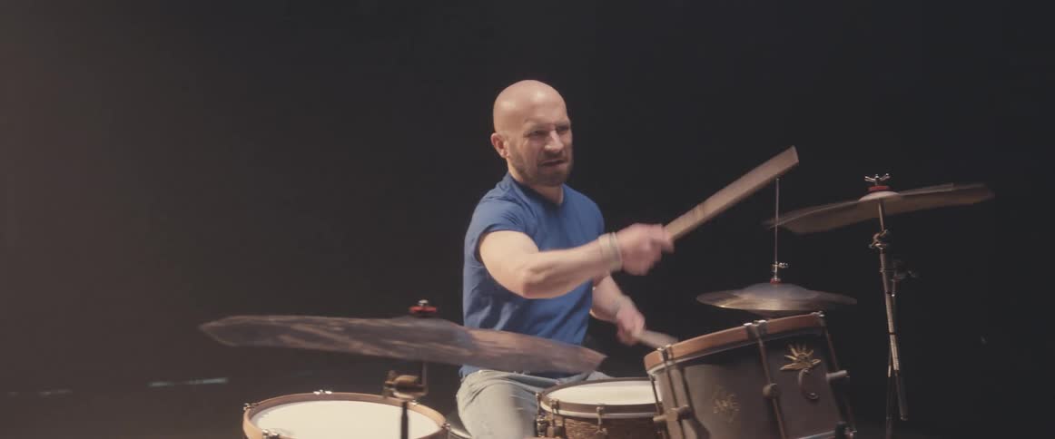 Bald muscular man playing drums on a stage under a spotlight