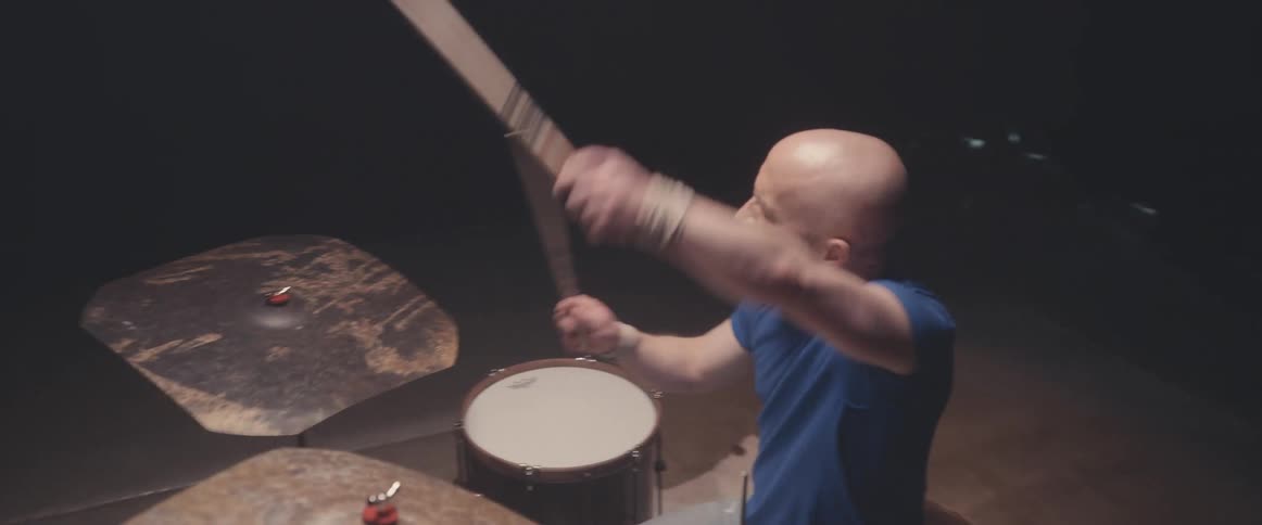 A musician is holding his drumsticks high in the air and keeping the rhythm playing the drums