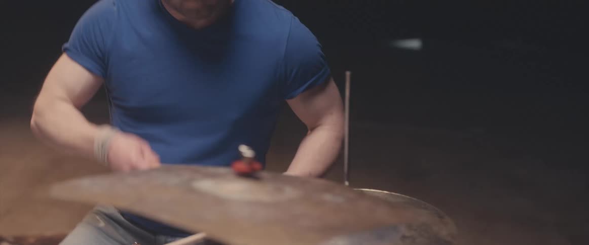 Bald male drummer with blue shirt jeans and beard plays drums in spotlight