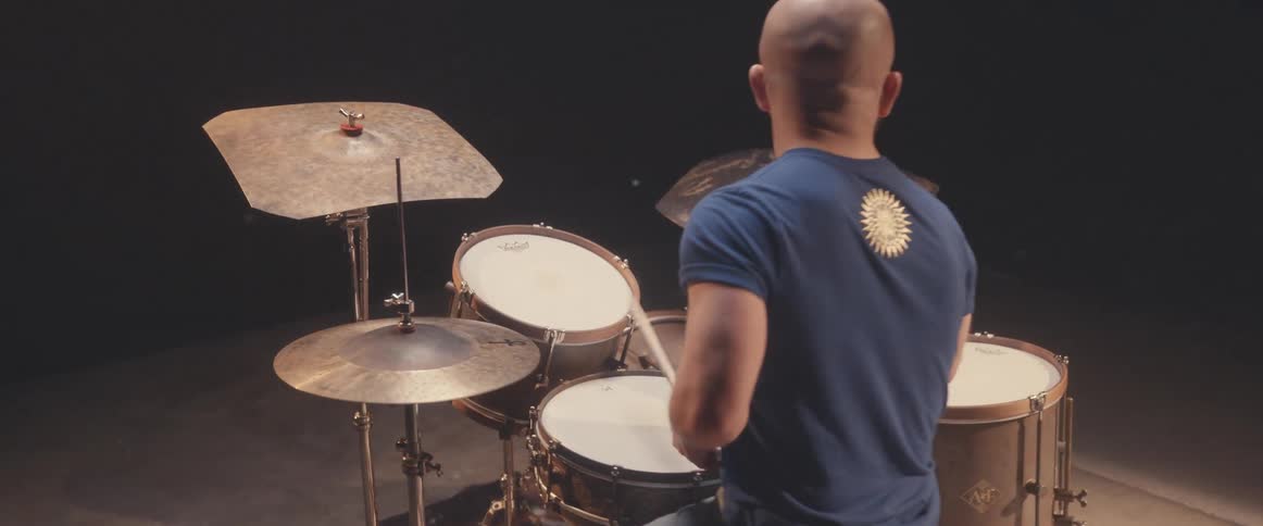 Bald muscular man playing drums on a stage under a spotlight