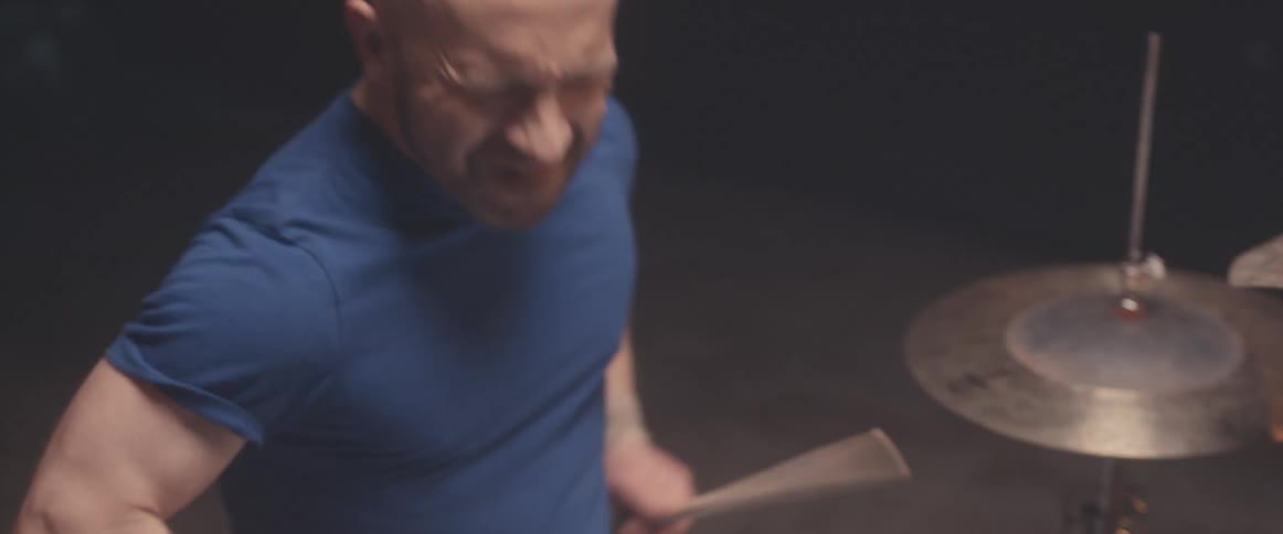 Bald muscular man playing drums on a stage under a spotlight