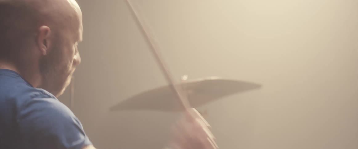 A man is holding drumsticks and playing the drums as a light shines above him