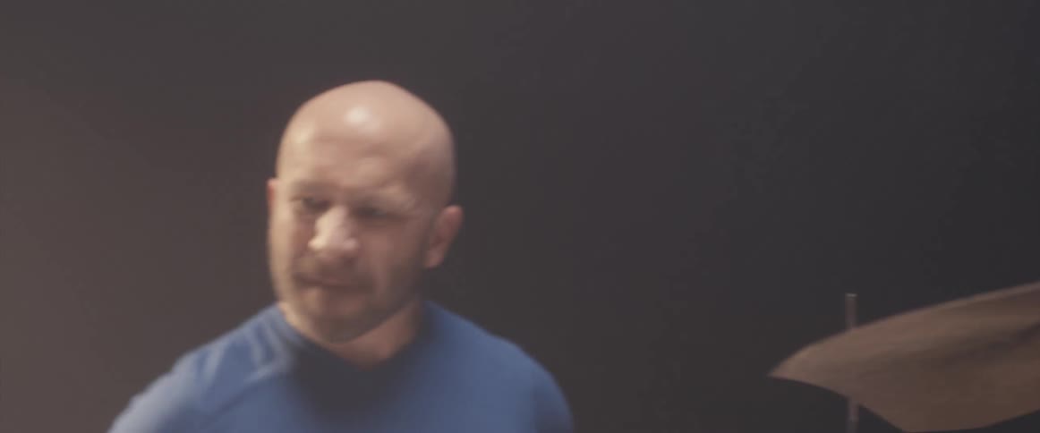 Bald muscular man playing drums on a stage under a spotlight