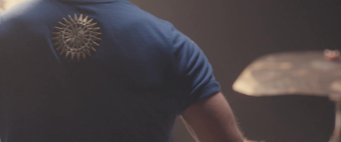 Bald male drummer with blue shirt jeans and beard plays drums in spotlight