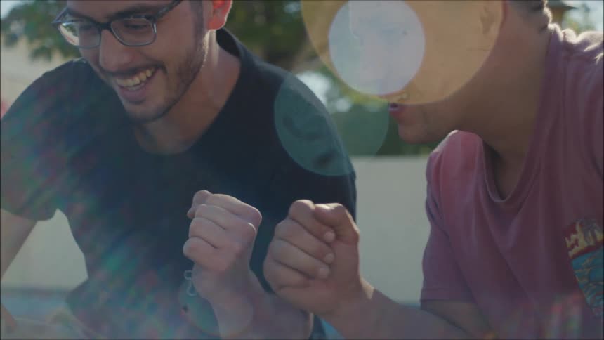 Two men laugh and fist bump while watching a smartphone together