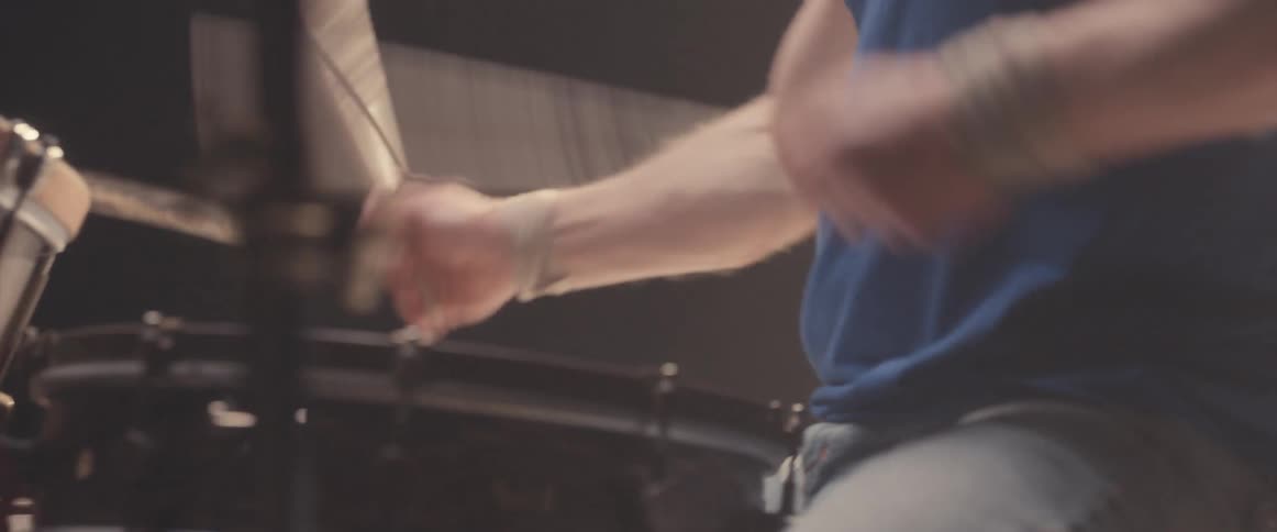 Bald muscular man energetically playing drums on a stage under a spotlight