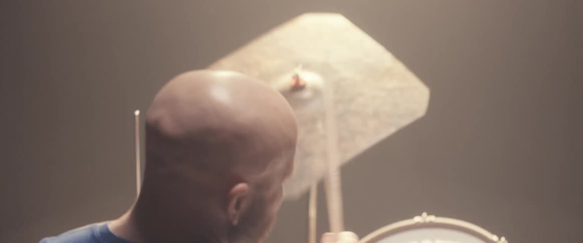 Bald muscular man playing drums on a stage under a spotlight