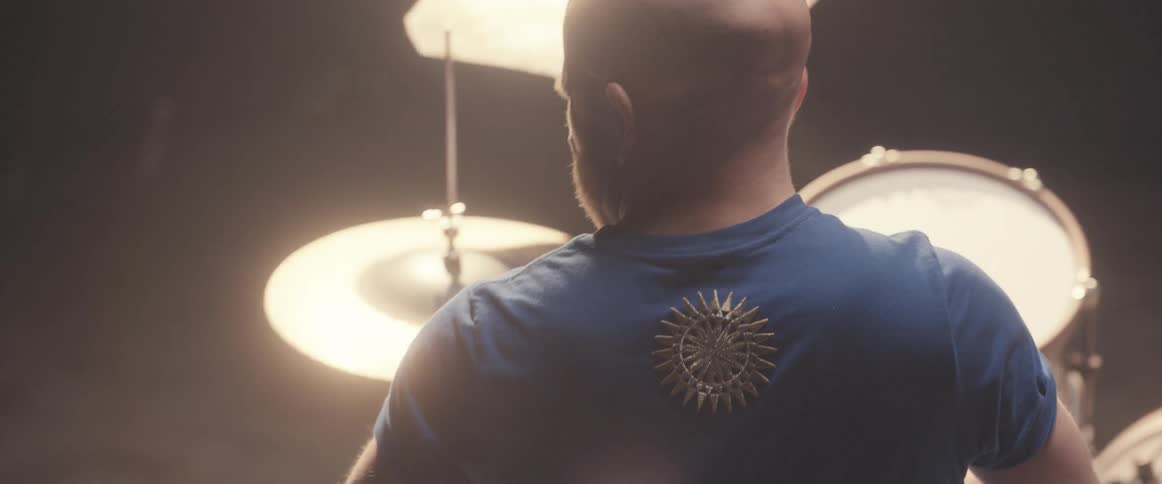 Bald male drummer with blue shirt and beard plays drums in spotlight