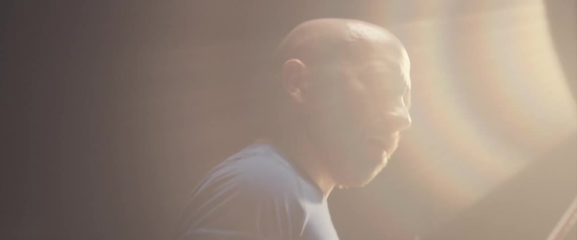 A man is holding drumsticks and playing the drums as a light shines above him