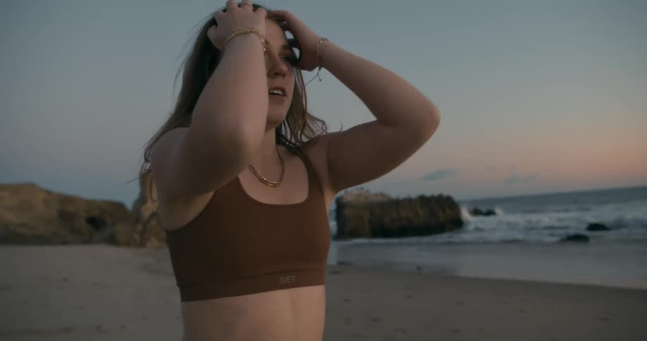Young woman wearing yoga clothes stretching on the sand beach at sunset next to the ocean