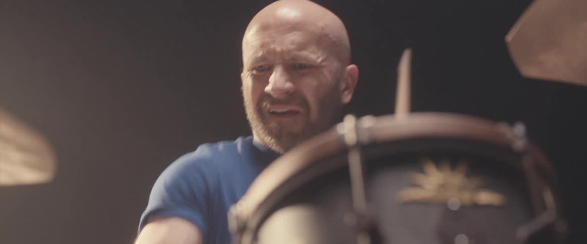 Bald muscular man playing drums on a stage under a spotlight