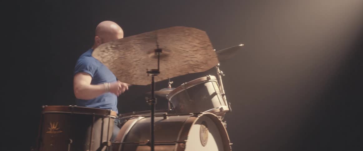 A man is holding drumsticks and playing the drums as a light shines above him
