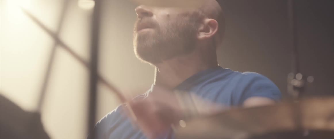 A man plays the drums under a bright spotlight