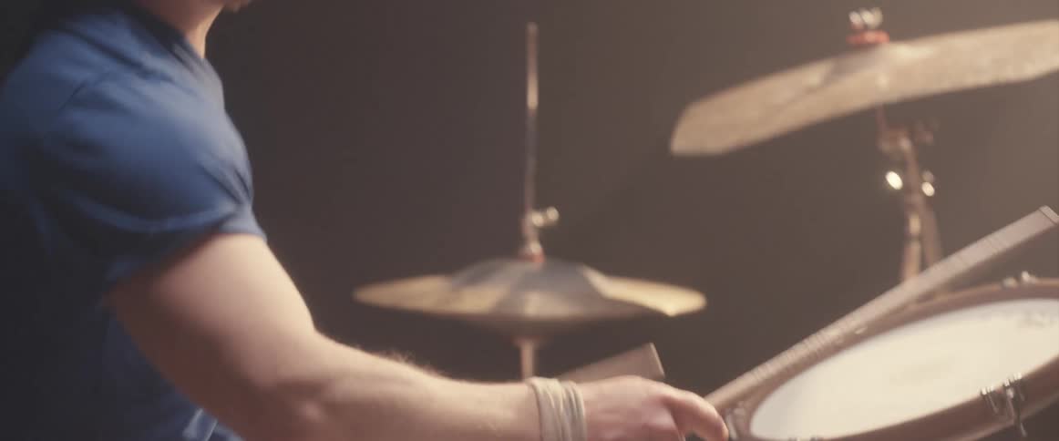 A musician is holding his drumsticks high in the air and keeping the rhythm playing the drums