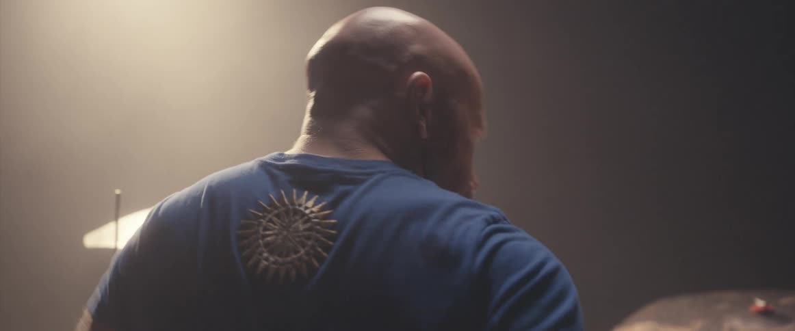 Bald muscular man playing drums on a stage under a spotlight