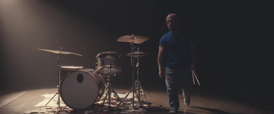 A drummer finishes his song, then stands up and walks away from his instrument carrying his drum sticks