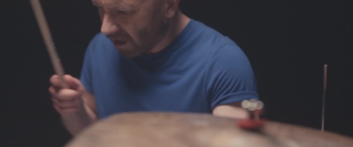 Bald male drummer with blue shirt and beard plays drums in spotlight