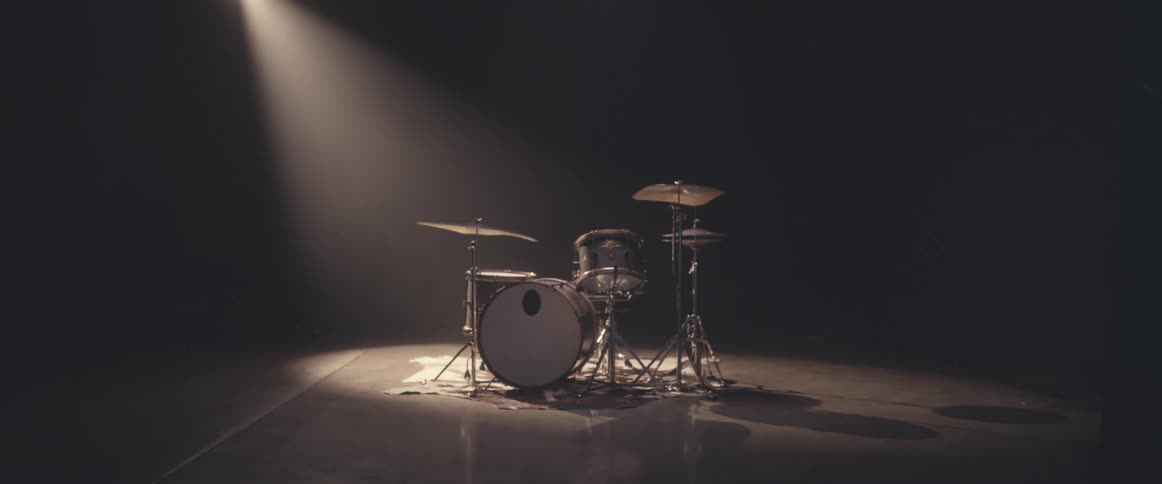 A light shines down on a drum set in an empty dark area