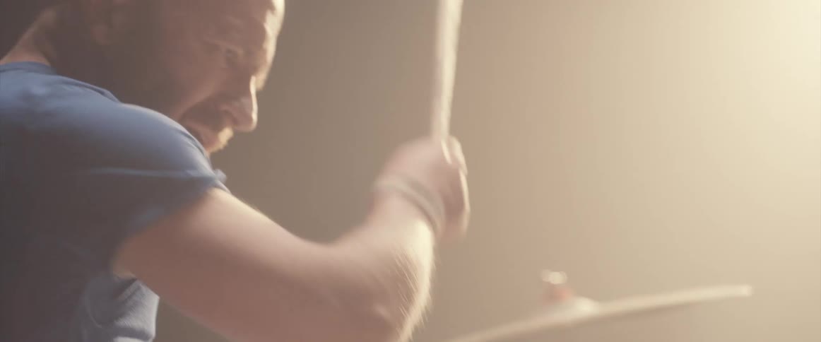 A man plays the drums under a bright spotlight