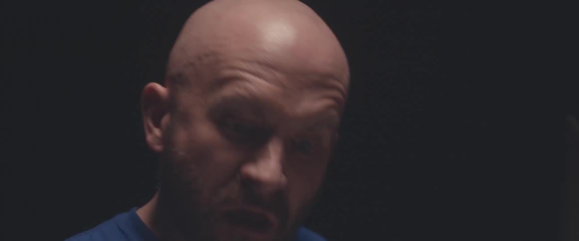 Bald male drummer with blue shirt and beard plays drums in spotlight
