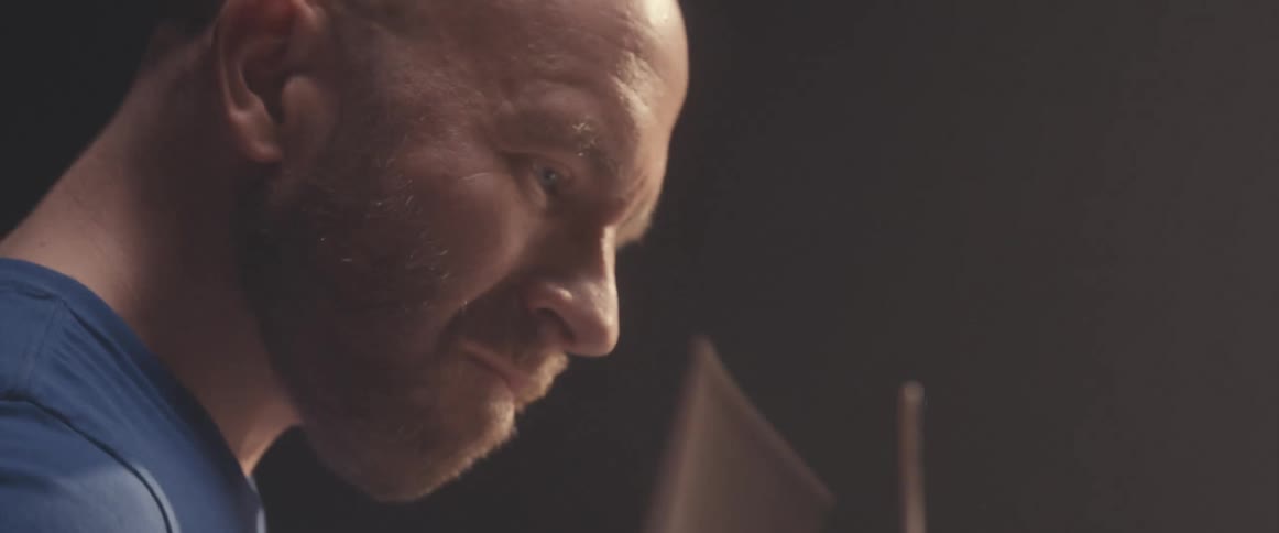Bald male drummer with blue shirt and beard plays drums in spotlight